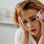Uplakana žena sedi i drži maramice pored očiju.