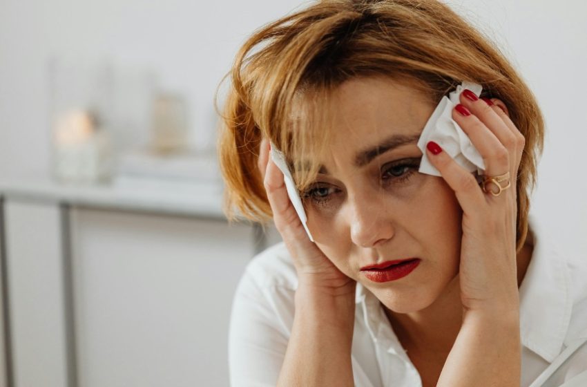 Uplakana žena sedi i drži maramice pored očiju.