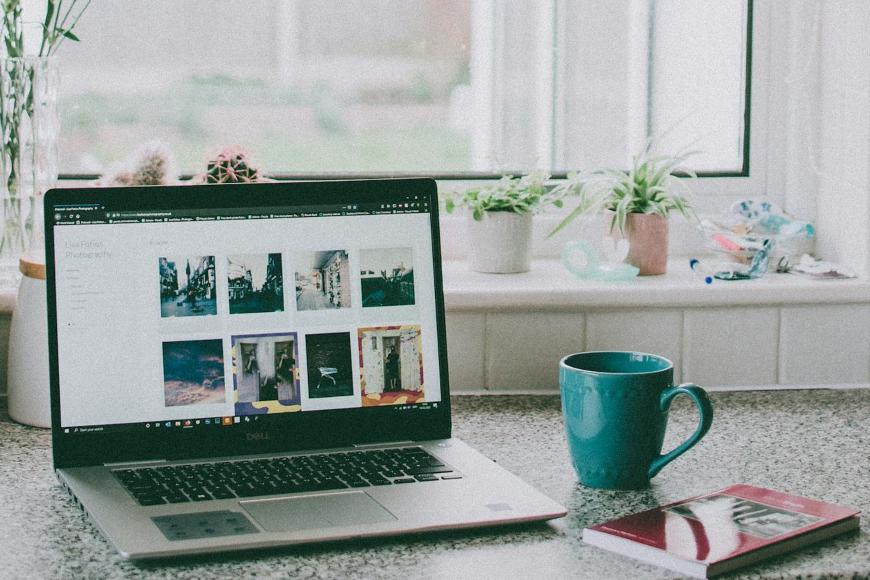 Radni sto na kojem se nalazi laptop, šolja i vaza sa cvećem.