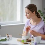 Devojka sedi za stolom i drži bočicu sa uljem u ruci