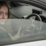 Devojka sedi u automobilu i drži volan