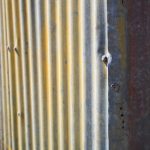 Talasasta limena ploča sa šrafovima i rđom.