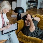 Čovek se drži za glavu dok leži na kauču i razgovara sa psihologom