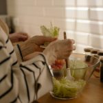 Ruke stavljaju listove zelene salate u staklenu činiju.