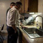 Dva muškarca stoje pored sudopere i gledaju mokru radnu površinu