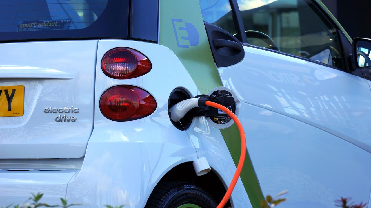 Beli električni automobil priključen na punjač sa narandžastim kablom