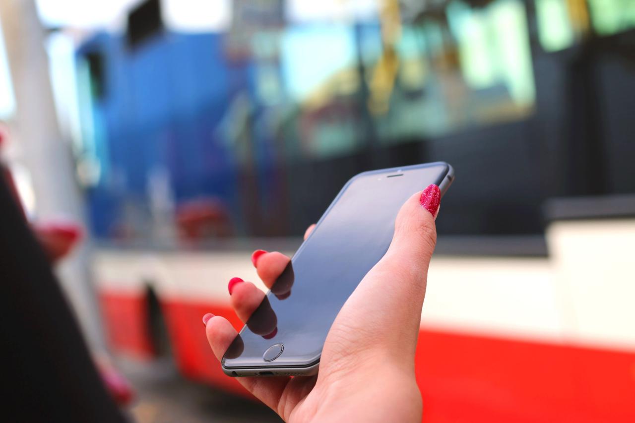 Ruka sa crvenim sjajnim lakiranim noktima drži mobilni telefon