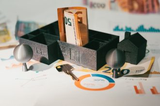 Na papiru stoji novac, ključ i maketa kuće.