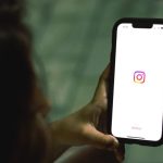 Devojka drži telefon na čijem ekranu se vidi ikonica aplikacije Instagram.