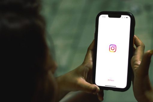 Devojka drži telefon na čijem ekranu se vidi ikonica aplikacije Instagram.